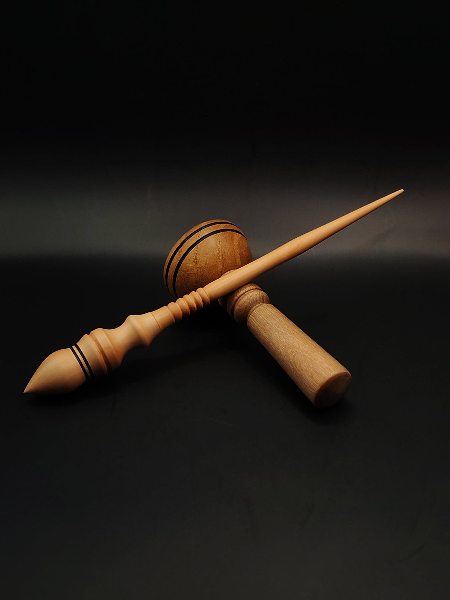 A handcrafted wooden support spindle with a smooth, polished finish, featuring a wide whorl and pointed tip, resting beside a matching wooden support bowl