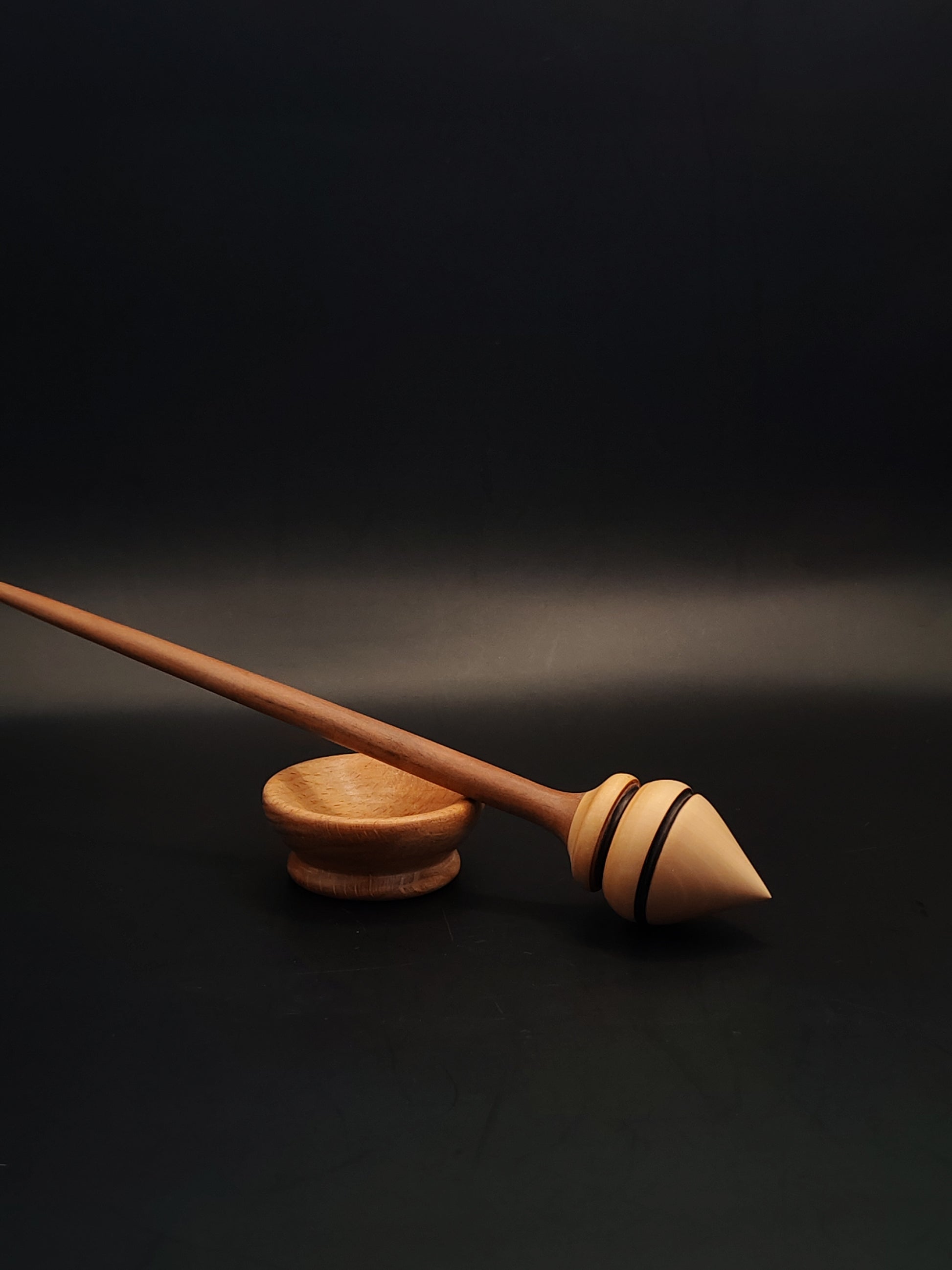 Handmade support spindle with plum shaft and pear wood whorl resting in beech bowl