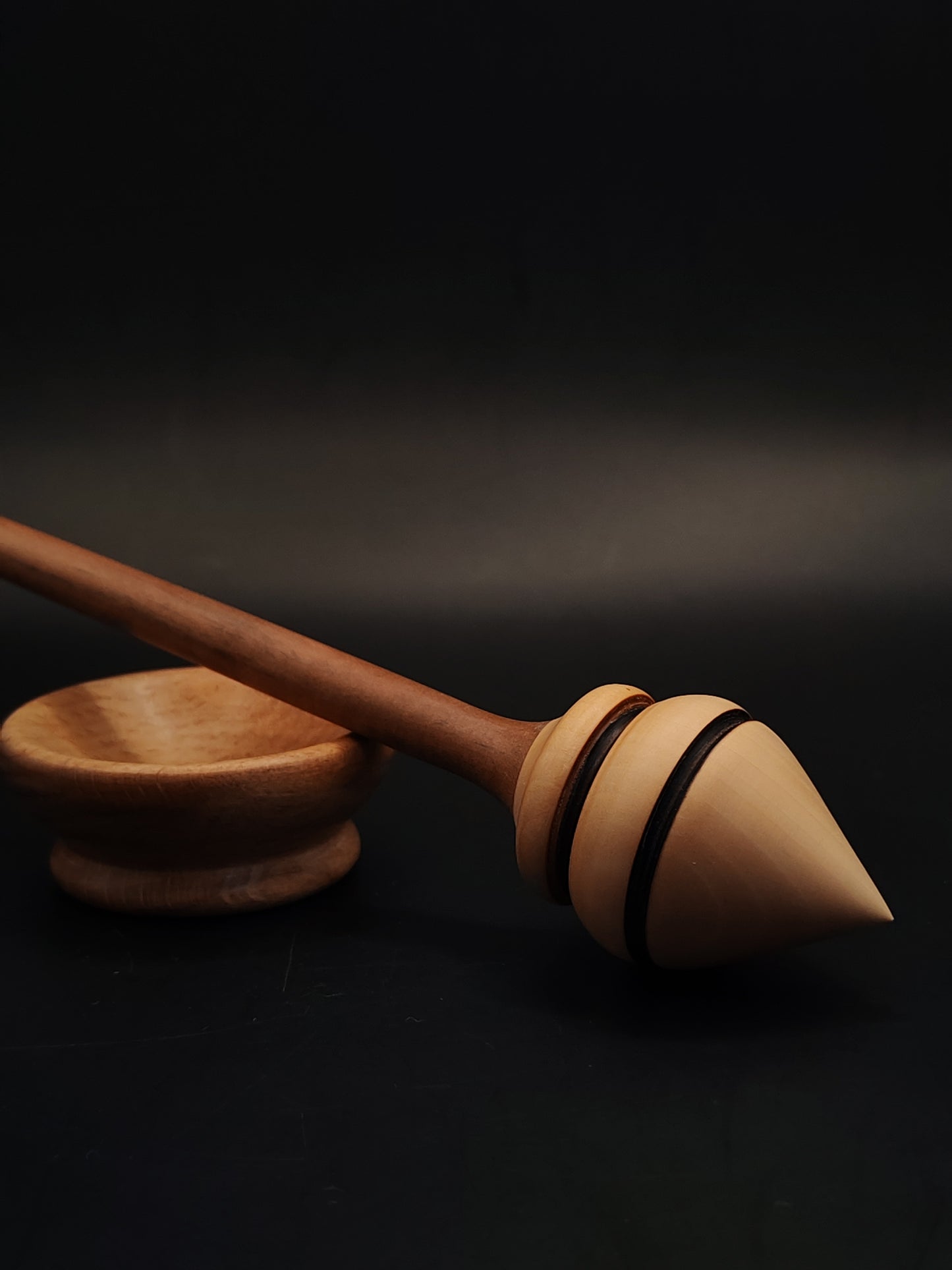 Side view of artisan spindle featuring slender plum shaft and light pear whorl