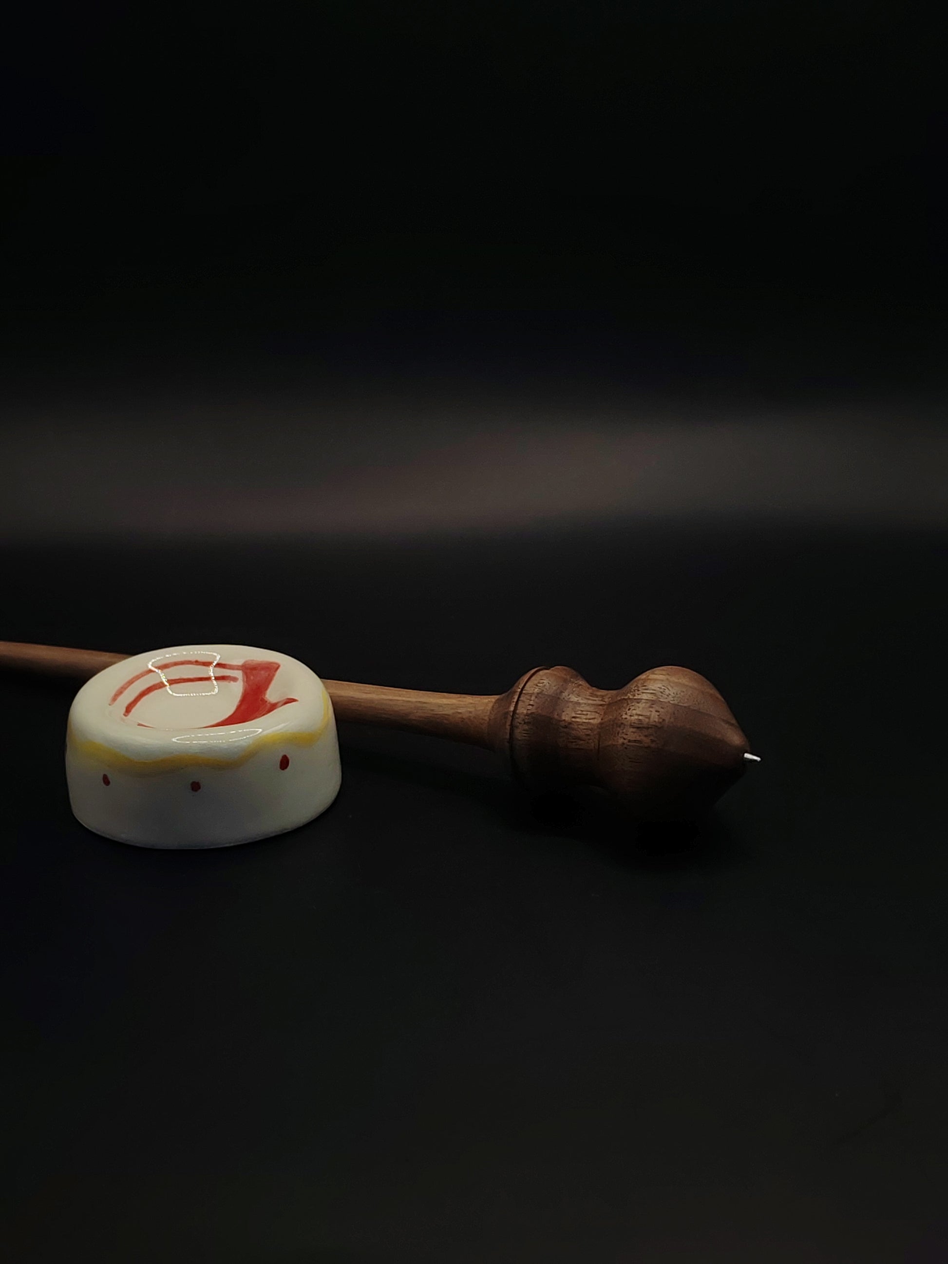 Handmade walnut support spindle with metal tip resting in ceramic spinning bowl