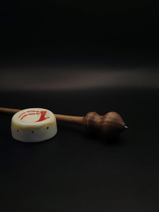 Handmade walnut support spindle with metal tip resting in ceramic spinning bowl