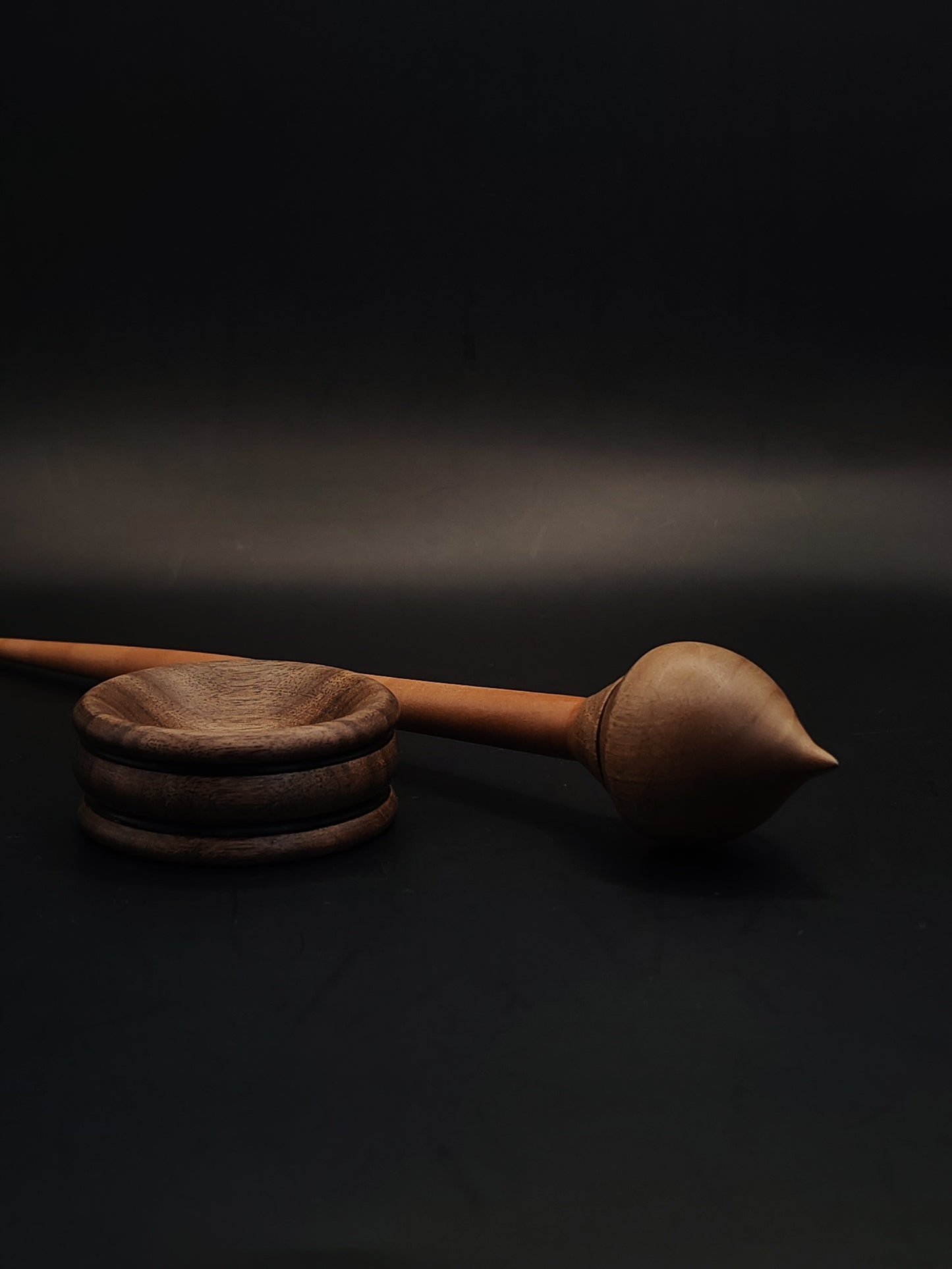 Side angle of artisan support spindle featuring plum shaft and smooth walnut whorl